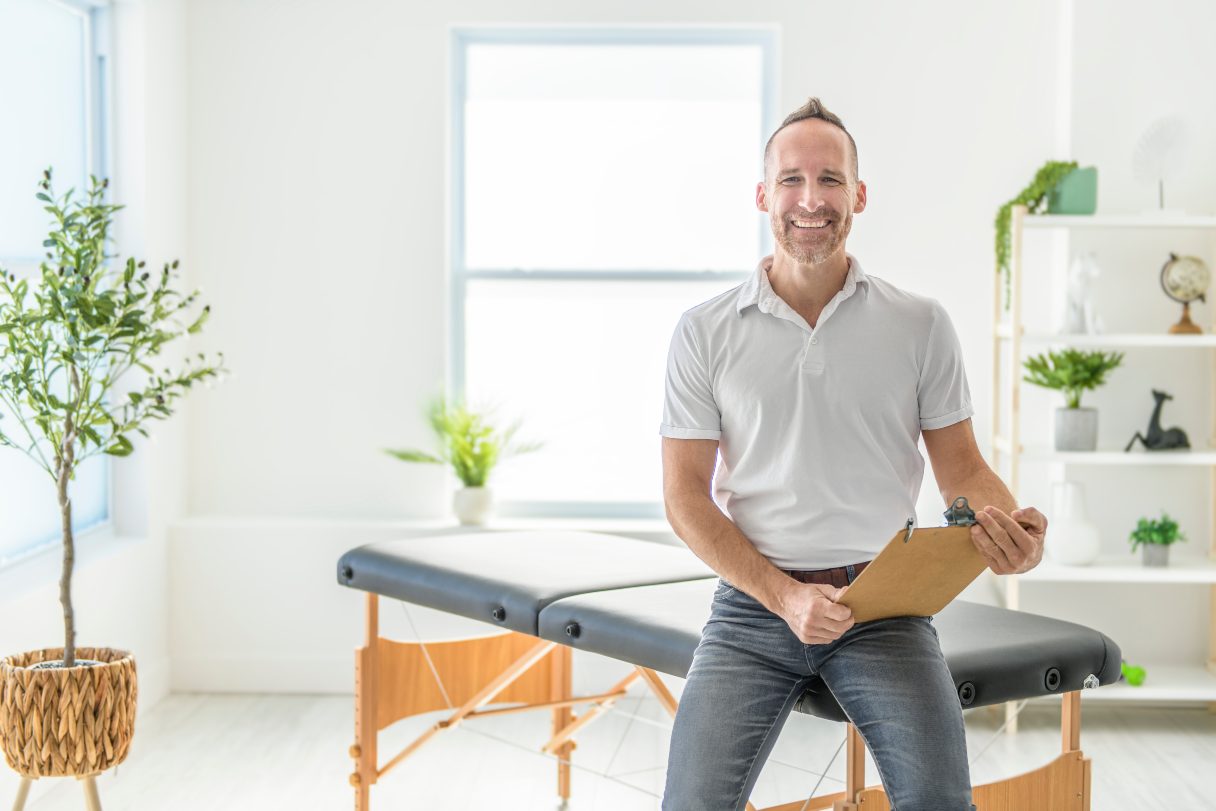 Chiropractor with clipboard sitting on chiropractic table